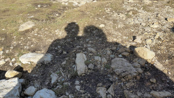 Schatten von zwei oder mehreren Personen, die zusammenstehen. Auf einer steinigen Wiese.